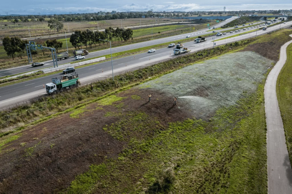 A hydroseeder truck hydromulching on the side of a freeway