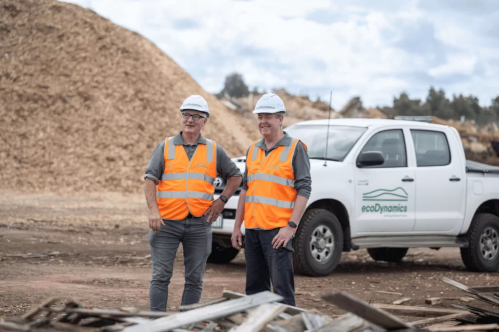 MossRock Mulch with two men looking into the distance and a giant recycled timber mulch pile behind them