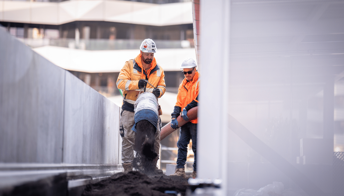 Two ecoDynamics workers are holding a blower hose from a blower truck to blow soil onto the ground up on level 9 of a building.