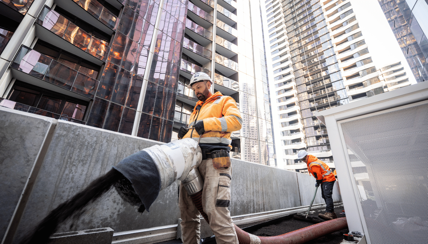 Two ecoDynamics landscaping workers on the 9th floor of a building using a blower hose to blow soil onto the ground. One is blowing and the other one is sweeping and flattening the soil.
